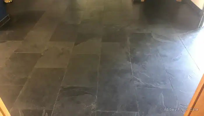 Thick buildup of discoloured floor wax along slate tile edges and grout